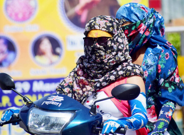 Women use scarves to cover their faces as they commute on a bike during a hot summer day